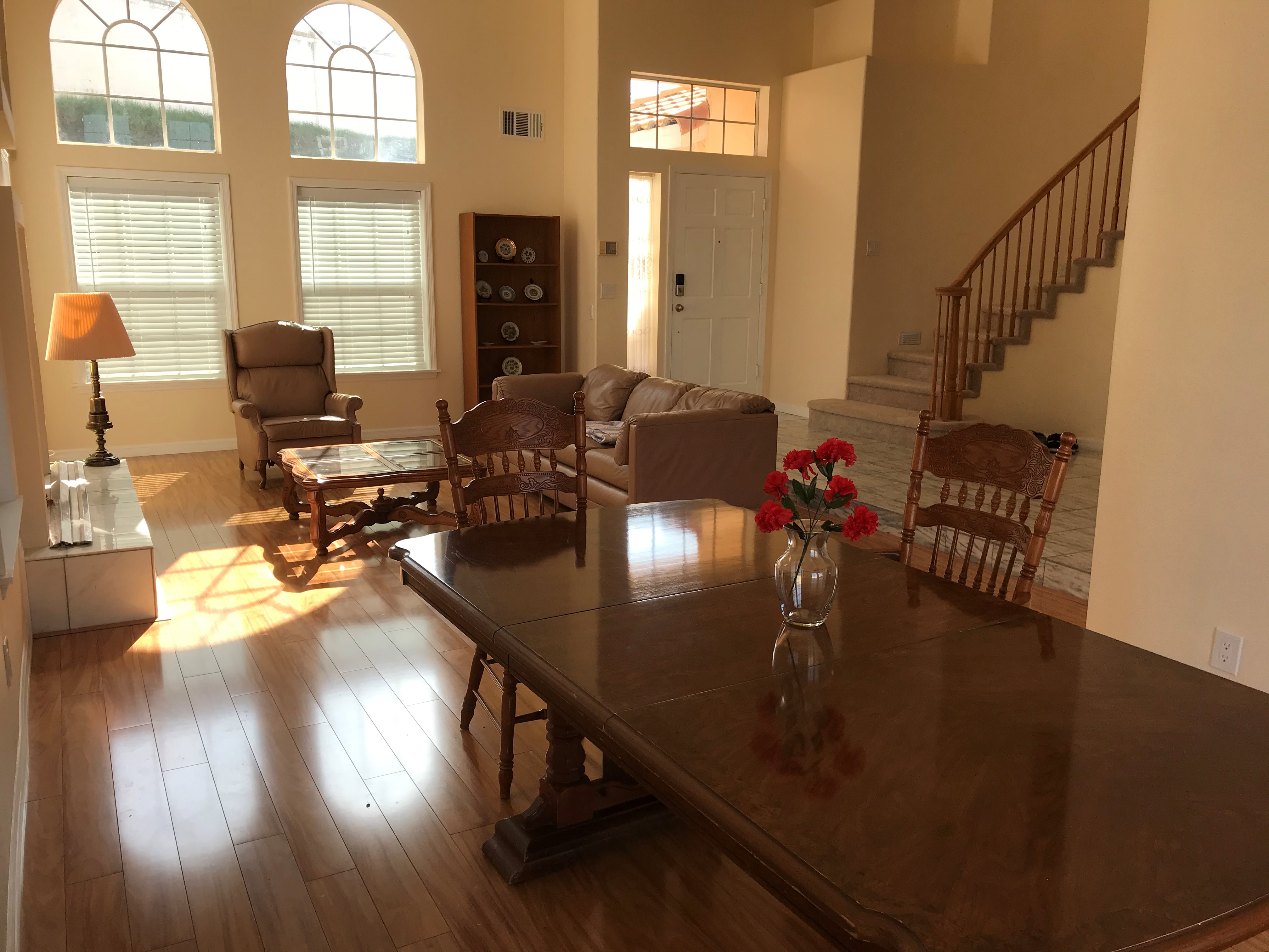 Formal living and dining room with hardwood floors, arched windows flooding natural light, and curved staircase