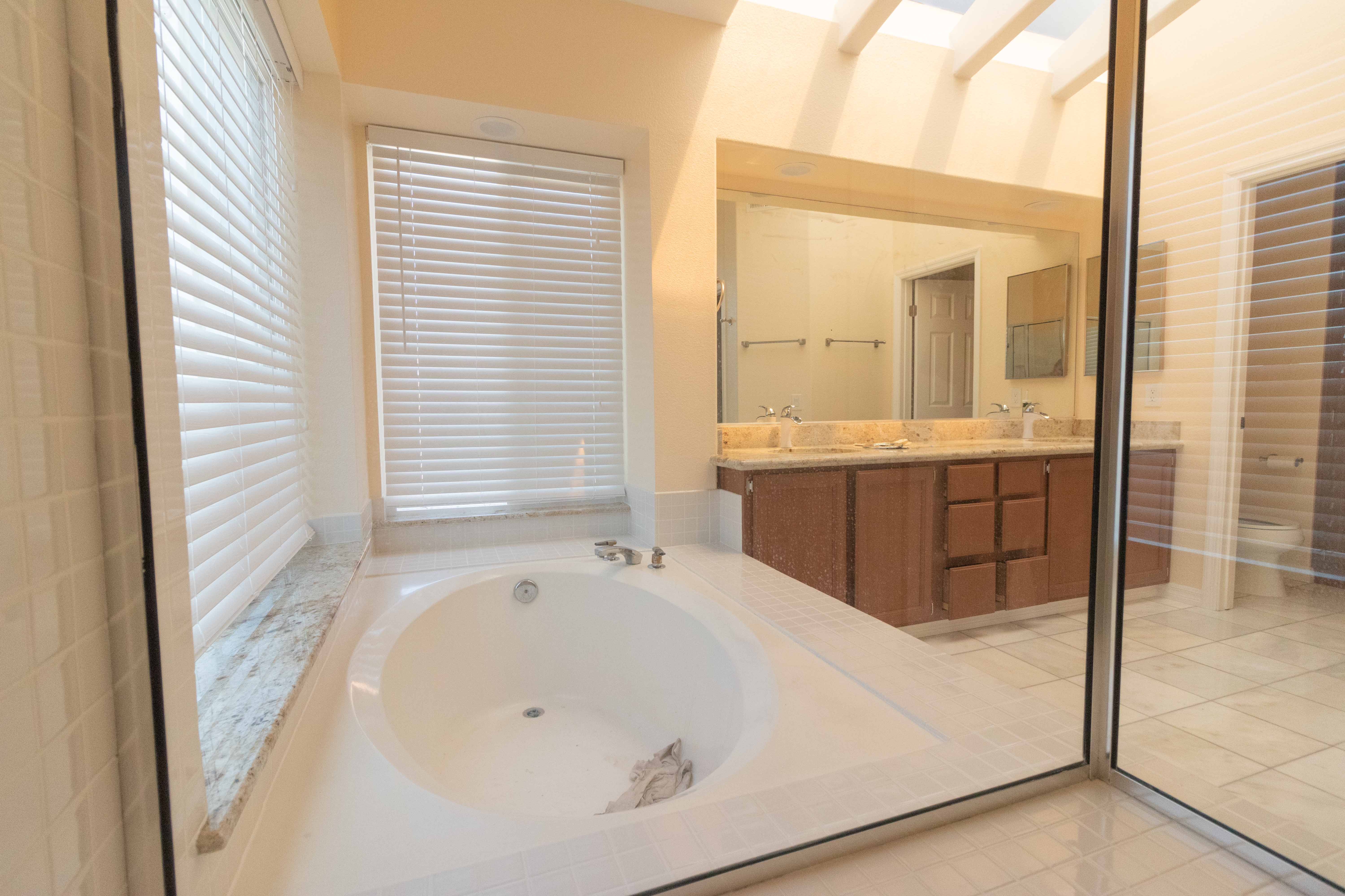 Master en-suite bathroom soaking tub with skylight above, double vanity and glass shower seen through glass door